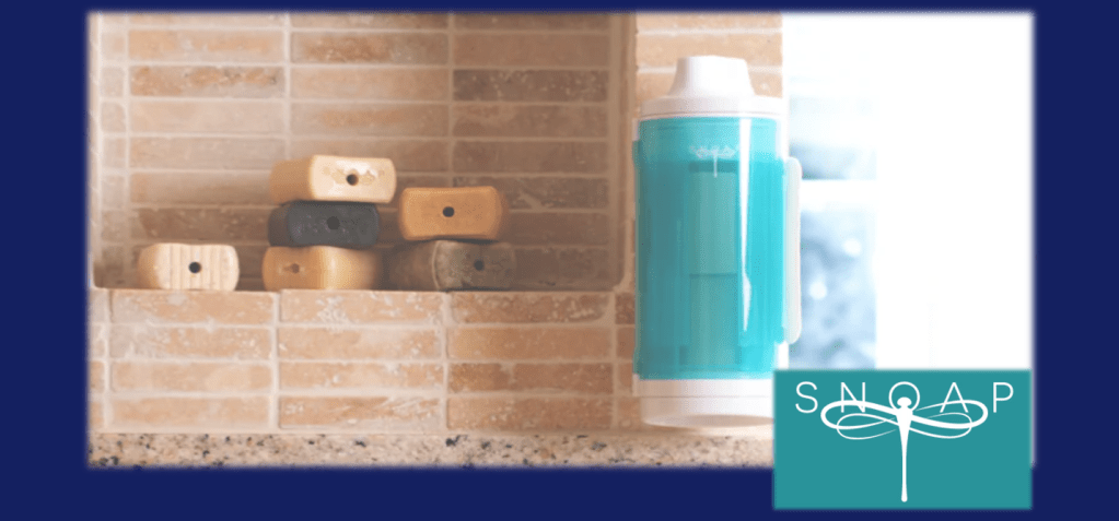 An image of 6 bars of Snoap's soap together with their patented Snoap grater.   Also the Snoap logo which looks like a fairy dragonfly.